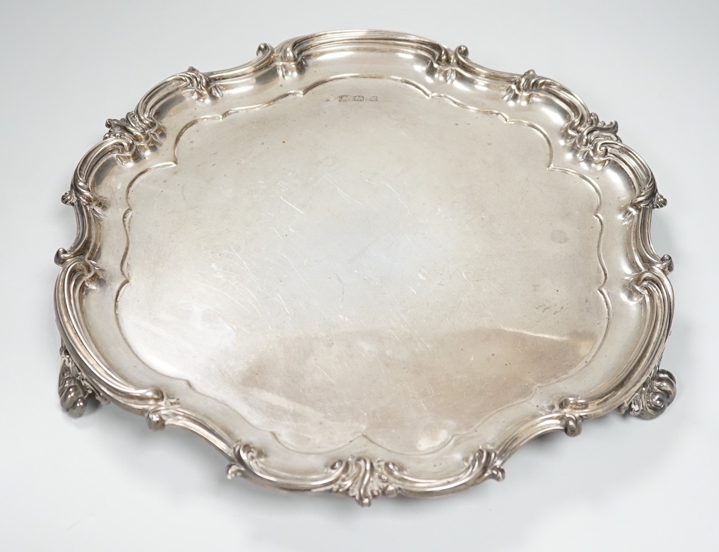 A George V silver salver by Elkington & Co, Birmingham, 1911, of shaped circular form with scroll border, on three scroll feet, diameter 37cm